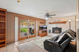 Tiled living area featuring a textured ceiling, ceiling fan, wooden walls, and a fireplace