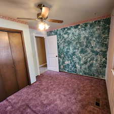 Unfurnished bedroom featuring carpet floors, ceiling fan, visible vents, and a closet