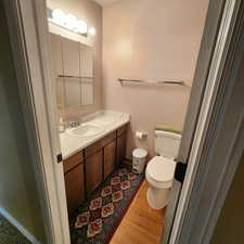 Half bathroom with vanity, baseboards, wood finished floors, and toilet