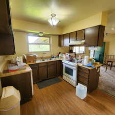 Kitchen featuring white electric range oven, a sink, light wood finished floors, light countertops, and under cabinet range hood