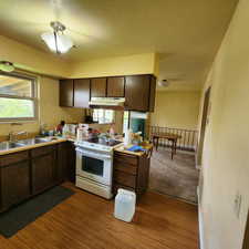 Kitchen featuring dark wood-style flooring, dark brown cabinetry, white range with electric cooktop, under cabinet range hood, and a sink
