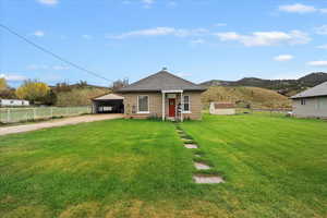 View of front facade featuring a front lawn, fence, dirt driveway, an outbuilding, and a carport