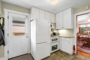 Kitchen with white appliances, light countertops, white cabinets, a ceiling fan, and light tile patterned floors
