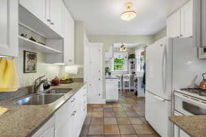 Kitchen featuring open shelves, light stone countertops, arched walkways, white cabinets, and a sink