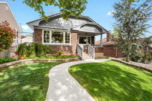 Bungalow-style house with brick siding, fence, covered porch, and a front yard