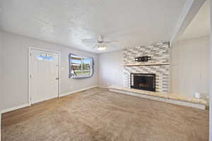 Unfurnished living room with ceiling fan, a brick fireplace, a textured ceiling, carpet, and baseboards