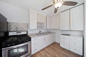 Kitchen featuring open shelves, gas stove, light countertops, a sink, and white cabinetry