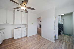 Interior space with light wood-type flooring, a brick fireplace, white cabinetry, and ceiling fan