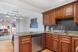 Kitchen with light wood-type flooring, dishwasher, a sink, light stone counters, and a peninsula