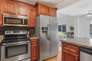 Kitchen with brown cabinetry, light wood finished floors, light stone countertops, and stainless steel appliances