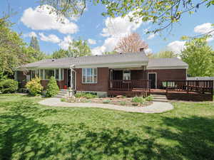 View of front facade featuring brick siding, a wooden deck, a chimney, and a front lawn