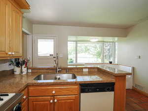 Kitchen with white dishwasher, a sink, range, brown cabinetry, and visible vents