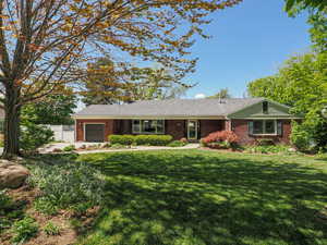 Ranch-style house featuring brick siding, an attached garage, fence, and a front yard
