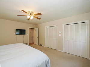 Bedroom featuring light colored carpet, multiple closets, a ceiling fan, baseboards, and visible vents