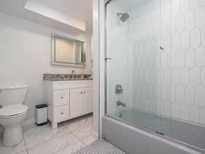 Bathroom with vanity, toilet, marble finish floor, baseboards, and shower / washtub combination