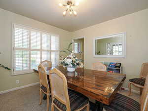 Carpeted dining space with baseboards and a notable chandelier