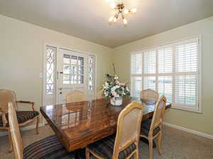 Carpeted dining room with a healthy amount of sunlight, baseboards, and a notable chandelier