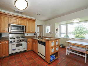 Kitchen with range with gas stovetop, a peninsula, dishwashing machine, stainless steel microwave, and a sink