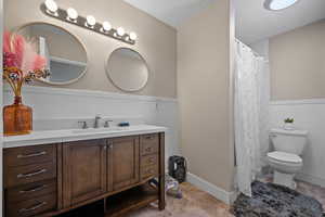 Full bathroom with vanity, curtained shower, toilet, a textured ceiling, and a wainscoted wall