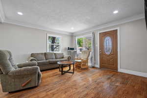 Living room featuring ornamental molding, recessed lighting, a textured ceiling, and wood finished floors