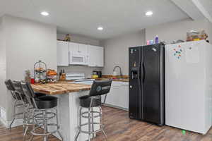 Kitchen featuring white appliances, wooden counters, white cabinetry, a peninsula, and a kitchen bar