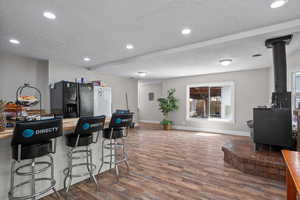 Kitchen featuring black fridge with ice dispenser, a wood stove, a textured ceiling, and wood finished floors