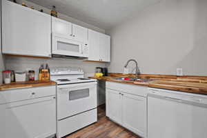 Kitchen featuring butcher block countertops, a sink, dark wood-style floors, and white appliances