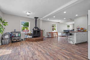 Living room with visible vents, a wood stove, a textured ceiling, and wood finished floors