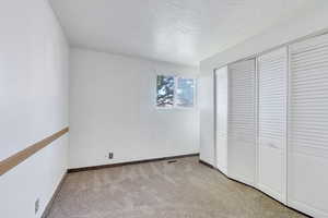 Unfurnished bedroom featuring baseboards, light carpet, a closet, and a textured ceiling