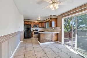 Kitchen with brown cabinetry, a peninsula, light countertops, a sink, and stainless steel appliances