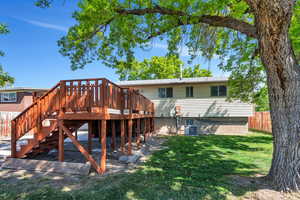 Rear view of house featuring a wooden deck, fence, stairs, a lawn, and central air condition unit