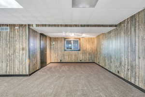 Finished basement featuring carpet floors, wooden walls, baseboards, and visible vents
