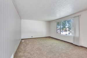 Carpeted empty room with a textured ceiling and baseboards