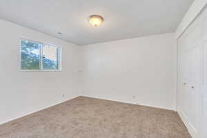 Unfurnished bedroom with a textured ceiling, visible vents, carpet, and a closet
