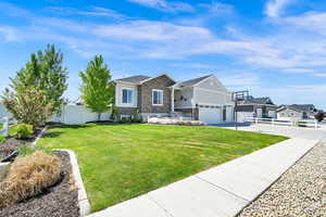 View of front facade with fence, a front lawn, stone siding, a gate, and concrete driveway