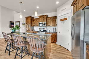 Kitchen with brown cabinets, appliances with stainless steel finishes, a sink, decorative backsplash, and light wood-type flooring
