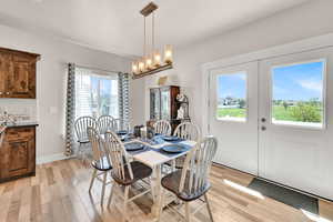 Dining room with light wood-style floors, a notable chandelier, and french doors