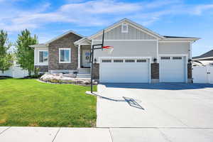 Craftsman-style house with an attached garage, a front lawn, stone siding, board and batten siding, and concrete driveway