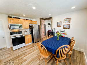 Kitchen with a textured ceiling, appliances with stainless steel finishes, tasteful backsplash, baseboards, and light wood finished floors