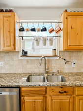 Kitchen with a sink, decorative backsplash, stainless steel dishwasher, and light stone countertops