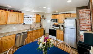 Kitchen featuring appliances with stainless steel finishes, decorative backsplash, a sink, and light wood-type flooring