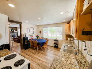 Kitchen featuring light brown cabinets, white electric range, a textured ceiling, a sink, and light wood finished floors