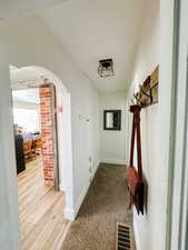 Hall with arched walkways, baseboards, visible vents, and light wood-type flooring