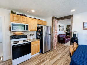 Kitchen with light wood-type flooring, freestanding refrigerator, range with electric cooktop, and tasteful backsplash