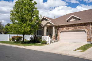 View of front of house featuring fence, roof with shingles, stone siding, a garage, and driveway