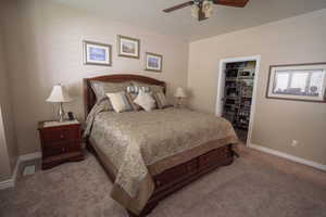 Carpeted bedroom featuring baseboards, ceiling fan, walk-in closet and ensuite.