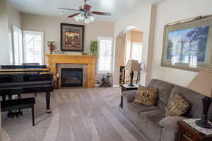 Carpeted living room featuring arched walkways, a ceiling fan, and a tile fireplace