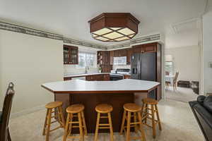 Kitchen with electric range oven, light countertops, a breakfast bar area, white microwave, and glass insert cabinets
