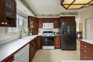 Kitchen with a sink, glass insert cabinets, white appliances, and light countertops