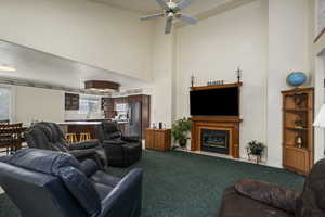 Living area with dark carpet, a ceiling fan, a glass covered fireplace, and a towering ceiling